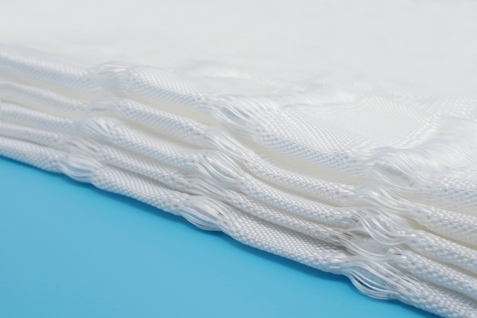 Close-up of layered geotextile mattress made from woven polypropylene fabric, showcasing its textured surface and connection points. The material appears strong and durable, designed for effective soil stabilization and erosion control. Visible seams indicate a high-quality finish, perfect for civil engineering projects. The mattress is displayed against a vibrant blue background for clear visibility.