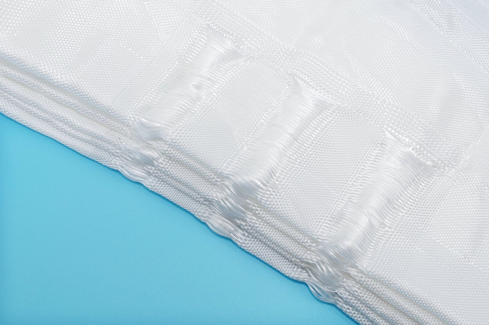 Close-up image of a geotextile mattress showcasing its woven texture and layered structure. The synthetic fibers are visible, indicating durability. The mattress is laid flat against a light blue background, emphasizing the material's white color and connection points.