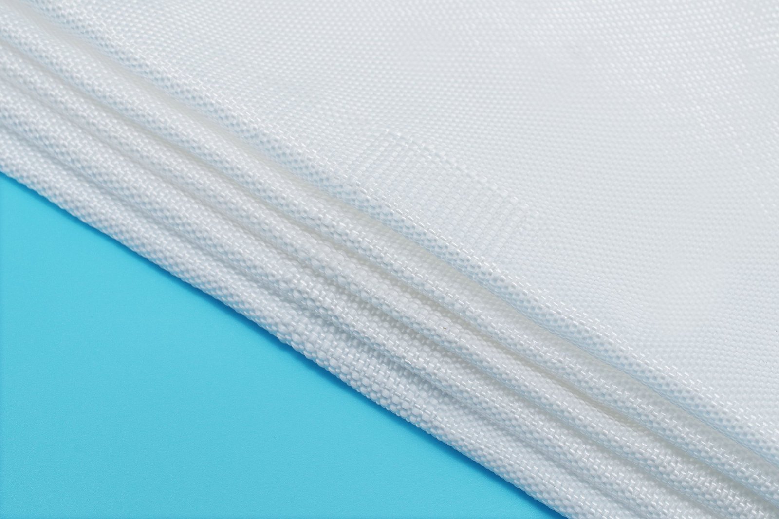 Close-up view of layers of geotextile mattress fabric showcasing its woven texture. The flat, white synthetic fabric, made from polypropylene, is neatly arranged, highlighting the product’s durability and permeability features essential for civil engineering applications.